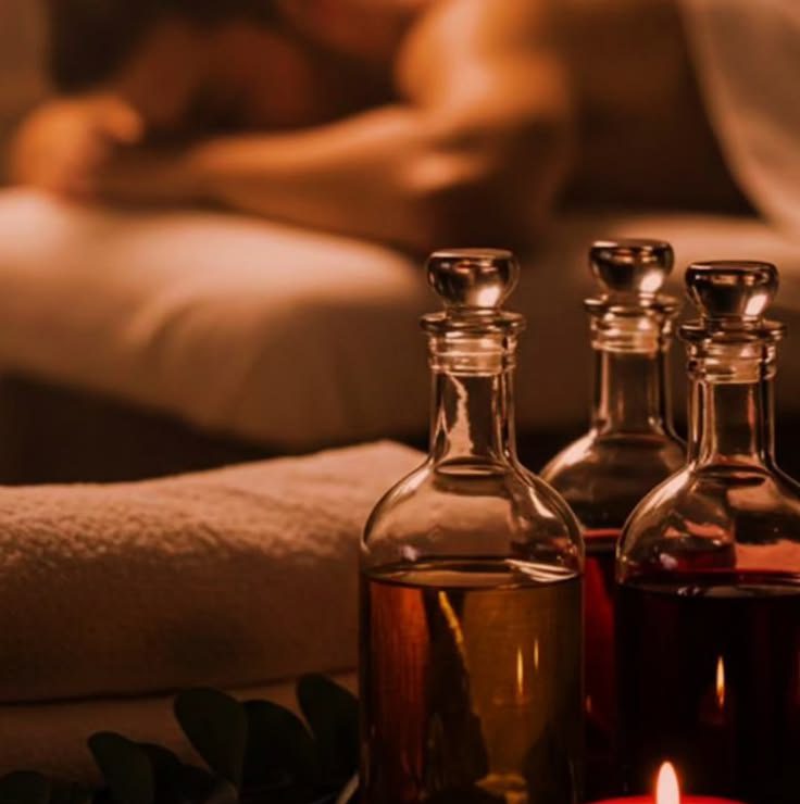 Glass bottles of massage oil beside a candle